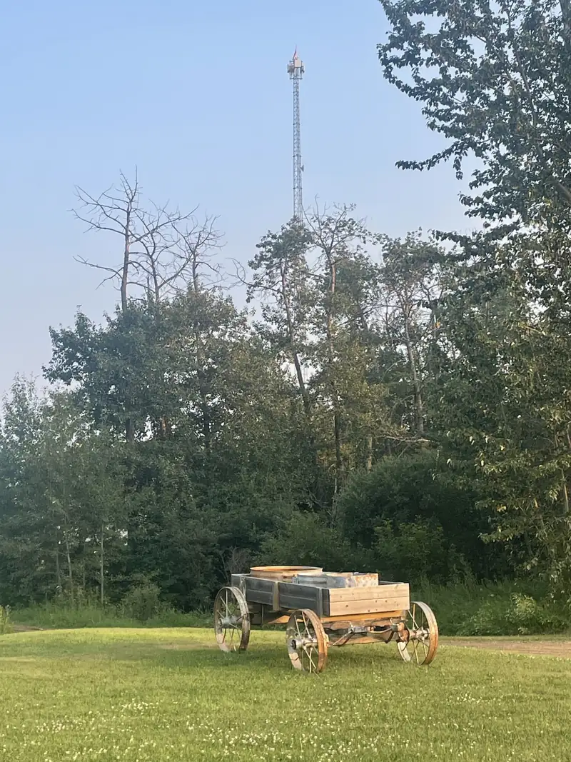 An Arrow tower above the trees behind an old wooden wagon